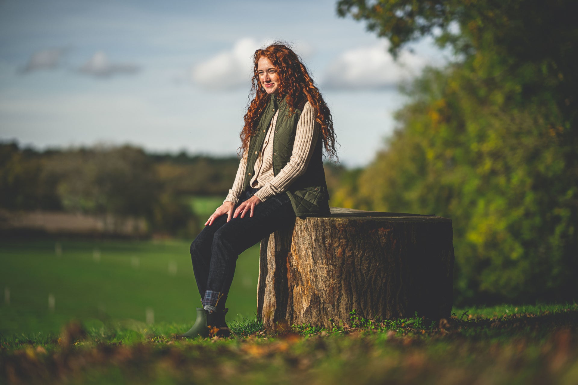 Woman in a green quilted gilet sitting on a tree stump